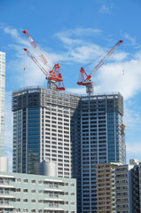 Fototapeta na wymiar Many tall buildings under construction and cranes under a blue sky near Sumida River at Tokyo, Japan