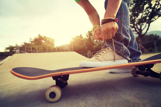 young skateboarder tying shoelace on skateboard at skatepark ramp