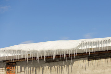 Obraz premium Plenty of ice icicles on edge of roof with blue spring sky