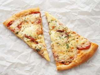 Two slices of freshly made pepperoni pizza upon baking parchment. Food background. Homemade pizza with tomatoes, hot sausages and soft cheese.