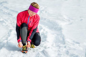 Fototapeta na wymiar Winter runner getting ready running tying shoe laces. Beautiful fitness model training outside. Copy space on snow.