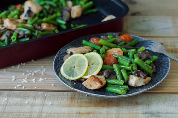 Portion of hot salad with green beans, chicken meat, mushrooms and cherry tomatoes served with lemon ans sesame seeds on wooden table