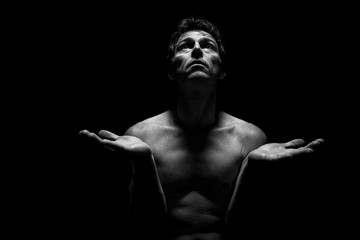 Fototapeta na wymiar Low key portrait of shirtless man in Yoga position. Black background, monochrome picture.