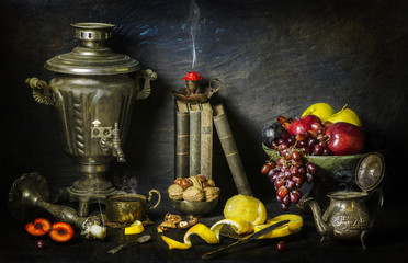 Classic still life with vintage books placed with old silver samovar,candlesticks,fresh fruits,cup of tea,tea pot and nuts on vintage background..