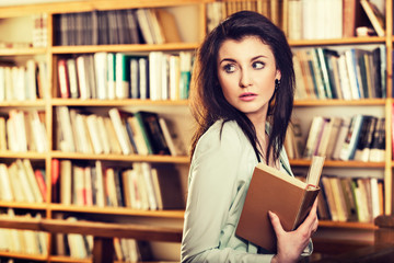 Young woman reading a book in front of bookshelves
