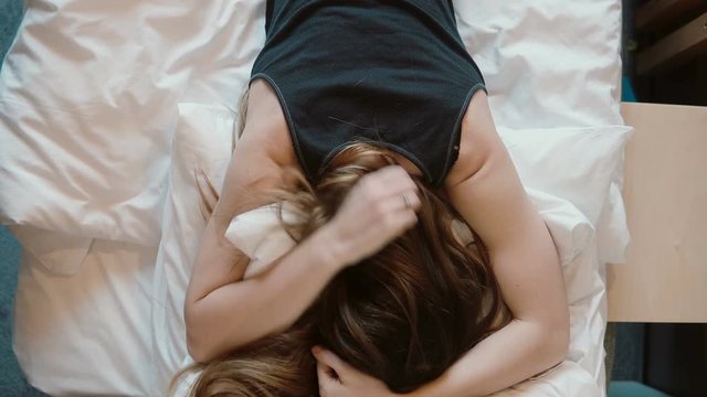 Tip view of angry woman falls face down on the bed. Girl beating her fist the pillows.