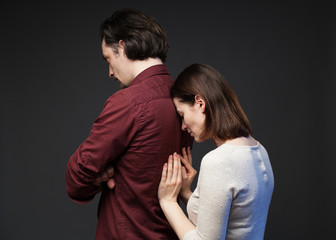 Misunderstanding in the family - the man is standing turned away with crossed hands, the woman is touching his back tenderly, gray background