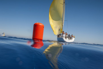 Sailing boat with yellow spinnaker and red buoy. Calm sea.