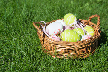 Easter painted pastel  color eggs with ribbon in basket  on green grass. Sunny day. Close up. Selective focus.