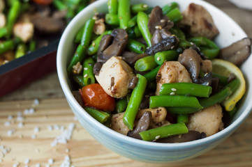 Bowl with hot salad: chicken breasts, green beans, red cherry tomatoes, mushrooms, sesame seeds