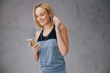 Beautiful young woman in sports wear and earphones is listening to music using a smartphone