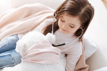 Obraz na płótnie Canvas Positive little girl examining fluffy toy with stethoscope