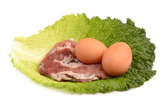 raw steak and eggs on a leaf of cabbage