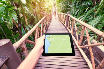 Traveling concept. Technology and adventure. Close up of hands holding tablet computer with map on screen in jungle.