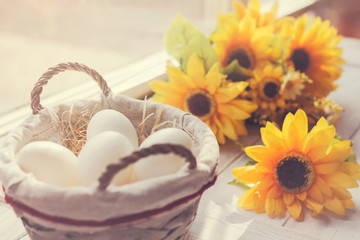 White eggs and bright yellow flowers iby the window, on light wooden table, Easter concept