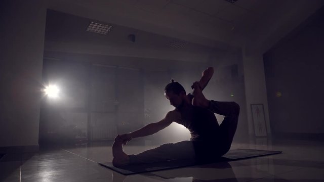 Flexible man stands on his hands in a gym.