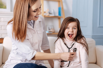 PoJoyful little girl sitting on the couch with professional doctor
