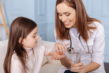 Cheerful doctor giving pills to little girl