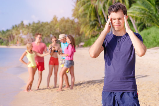 Stress and headache. Young man feeling bad while his friend enjoying beach party.