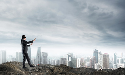 Young businessman in blindfold walking carefully and cityscape at background