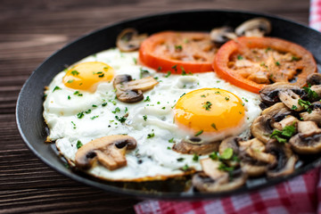 Fried eggs with mushrooms and tomato on dark wooden table - obrazy, fototapety, plakaty