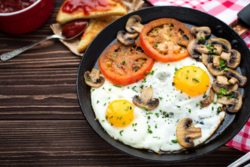 Fried eggs with mushrooms and tomato on dark wooden table