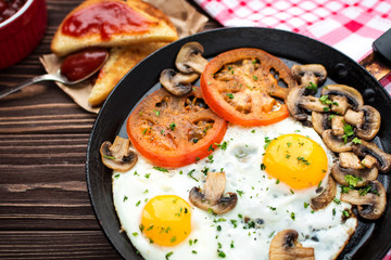 Fried eggs with mushrooms and tomato on dark wooden table