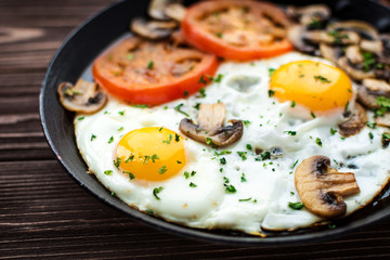 Fried eggs with mushrooms and tomato on dark wooden table