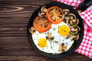 Fried eggs with mushrooms and tomato on dark wooden table