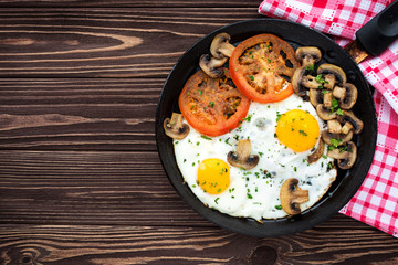 Fried eggs with mushrooms and tomato on dark wooden table