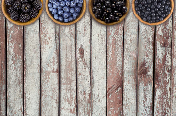 Black and blue berries. Blackberries, blueberries, currants and blueberries in a wooden bowls. Berries at border of image with copy space for text. Top view.