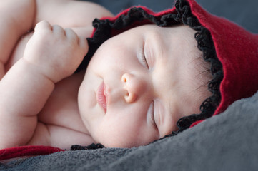 Newborn baby closeup in a red cap. Close-up portrait of a beautiful sleeping baby.  Photo with...