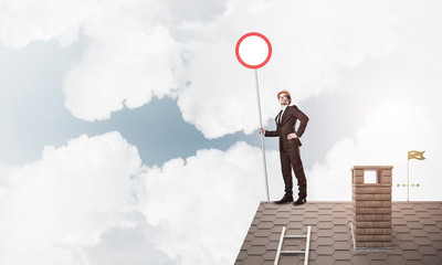 Caucasian businessman on brick house roof showing stop road sign