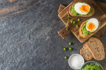 Baguette with mashed green peas, eggs and mint. Dark background.
