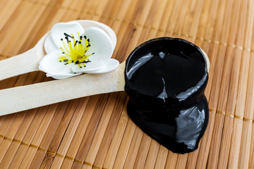 The black substance in a wooden spoon on a background of bamboo. Black mask