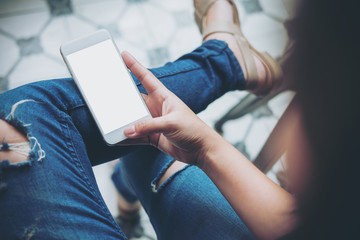 Mockup image of hand holding white mobile phone with blank white screen on thigh with a vintage...