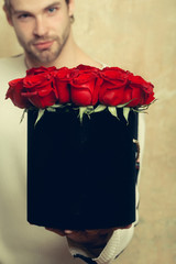 bearded man holds red rose box on textured wall