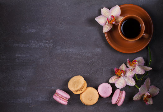 Coffee, orchids and cake macaron or macaroon on gray background from above. Flower, drink and coockie still life. Flat lay, top view