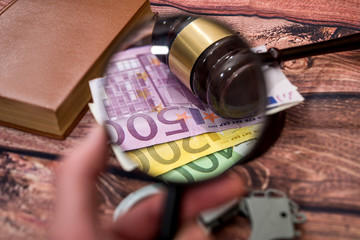 magnifying glass with euros, hammer, handcuff and book.