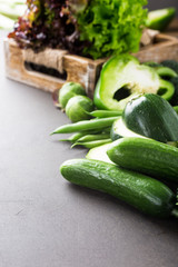 Mini cucumbers with assorted green vegetables, salad, broccoli, peas and Brussels sprouts on brown stone table top. Healthy food concept with copy space.