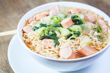 Instant Noodles with sausage with Pak Choy or Chinese Cabbage in white bowl and Plate on wooden table