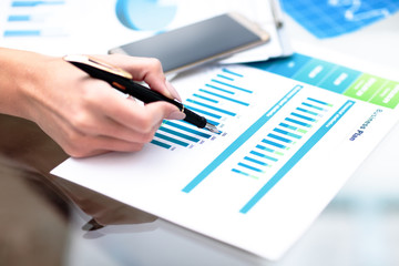 Close-up of businessman hand with pen explaining a financial plan to colleagues at meeting