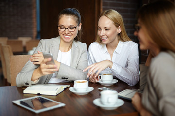 Interested females looking at data in smartphone while sitting in cafe