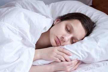 Girl brunette sleeping in her bed on white pillow