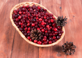Fresh cranberries in a small basket on a wooden background