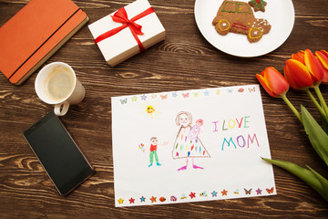 Happy mothers day card made by a child and a coffee cup on a wooden background of a table.