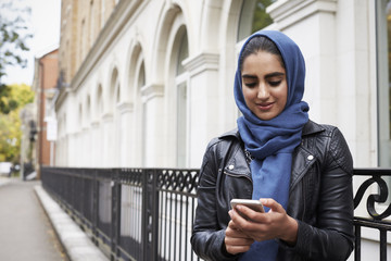 British Muslim Woman Using Mobile Phone In Urban Setting