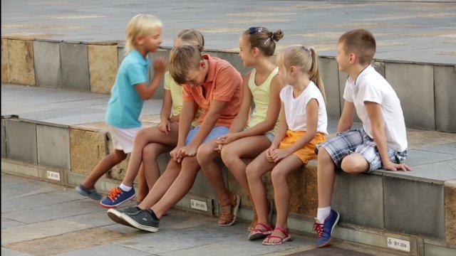 Group of children sitting on bench and sharing secrets outdoors