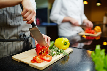 Female in uniform cutting fresh pepper and herbs for salad