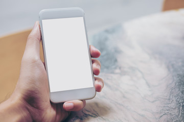 Mockup image of hand holding white mobile phone with blank white screen on marble table in cafe